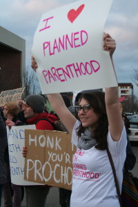 A woman holds an "I heart Planned Parenthood" sign. 